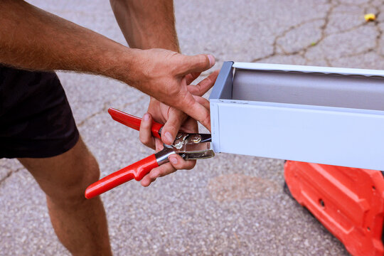 Builder is using clamps to hold metal gutter piece while fixing it in workspace outside