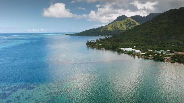 Moorea island displaying its vibrant blue ocean and clear lagoon water with visible coral reefs along the coastline. Complemented by dense tropical vegetation covering the dramatic mountain landscape