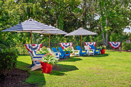A 4th of July patriotic backyard setup with red white and blue umbrellas, Adirondack chairs, and American flags.