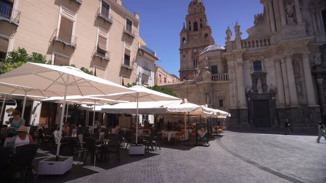 View of cafes and Cathedral of Murcia in Placa del Cardenal Belluga on a sunny day, Murcia, Murcia Region, Spain