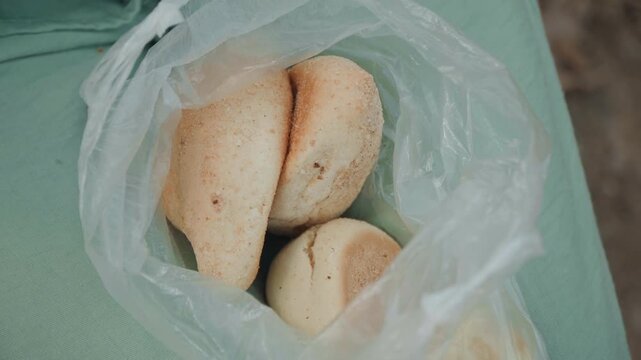 Close up of bread rolls in plastic bag on green fabric with soft lighting. scene shows baked goods inside clear packaging highlighting texture and casual presentation details