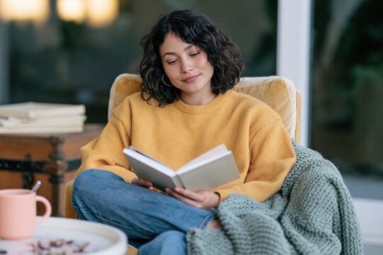 Closeup portrait of a young woman reading a book in a yellow sweater on a knitted blanket for calm lifestyle and relaxation wallpaper