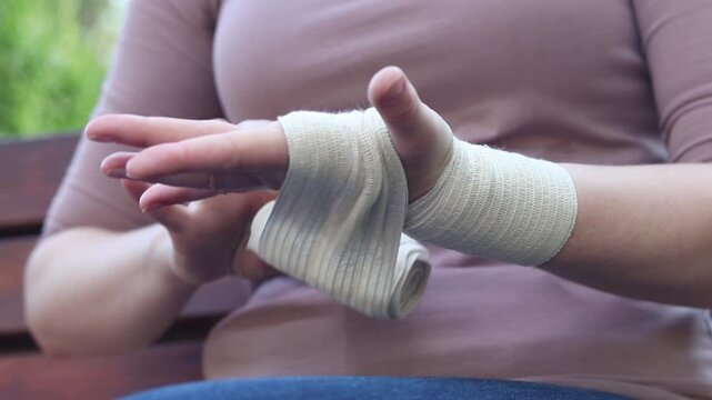 Injured hand of a patient with an elastic bandage on the wrist on a blurred natural background. Close-up of a female hand tightly bandaged with a medical elastic bandage to fix the joint