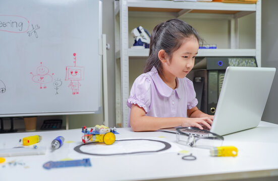 Asian girl student programming robot arm project while typing on laptop computer for stem education in classroom setting for learning technology and science concept