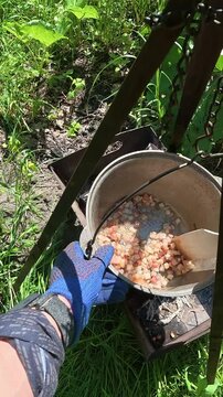 Man in gloves cooking campfire food in cauldron