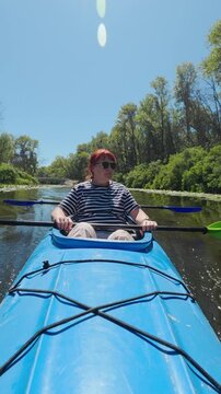 Mature woman holding paddle sitting in blue double kayak on river during summer adventure vacation