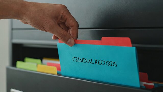 Criminal records file being pulled out of a filing cabinet drawer by a person in an office setting.
