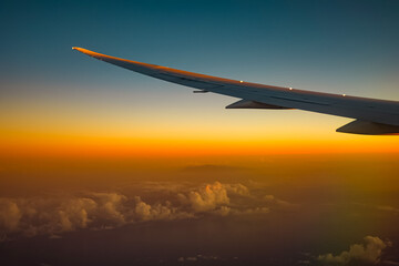 飛行機の窓から見下ろす夕焼けの鮮やかなグラデーションと雲海 © YUSUKE SAKAI