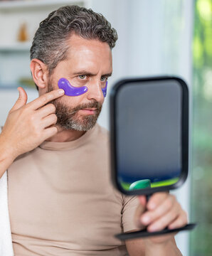 Eye patch. Beauty skin cosmetology of man with patch. Man use eye patch. Vitamin collagen patches. Beauty man face with under eye collagen pads hold mirror