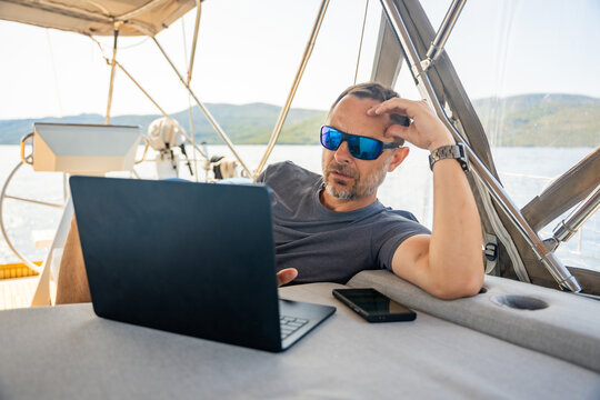 Focused man working on laptop aboard a sailing yacht. Productive remote office in a unique travel environment.