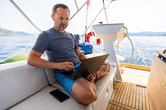 Focused man working on laptop aboard a sailing yacht. Productive remote office in a unique travel environment.