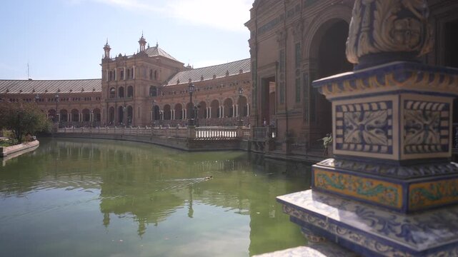 View of Plaza de Espana reflecting on moat from tiled bridge on a sunny day, Sevilla, Andalusia, Spain