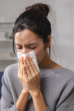 woman sneezing into tissue while feeling sick at home, showing respiratory symptoms and illness. allergy, cold, sneezing, tissue, sickness. Allergy and cold concept.