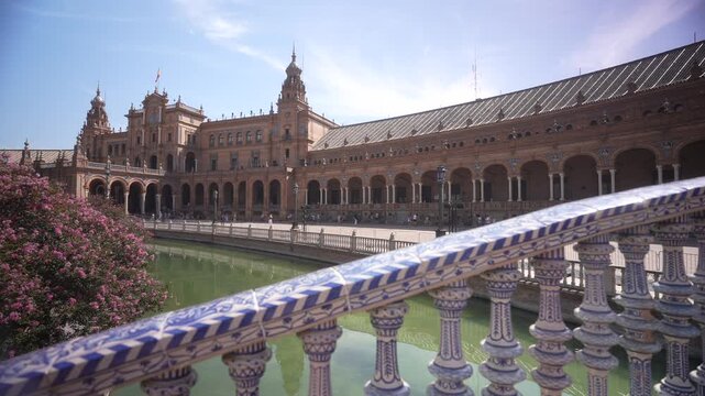 View of Plaza de Espana reflecting on moat from tiled bridge on a sunny day, Seville, Andalusia, Spain