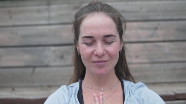 Close-up of a beautiful young woman practicing yoga with hands in namaste pose, eyes closed, and a peaceful smile. Wellness, meditation, mindfulness, relaxation, and healthy lifestyle concept