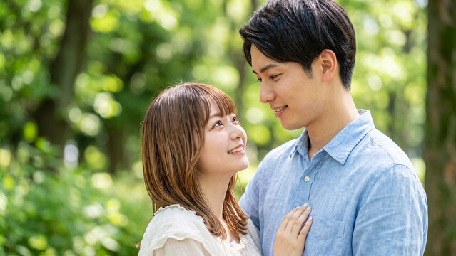 Young Asian couple in love smiling and looking at each other in a lush green park during summer, romantic relationship and lifestyle concept