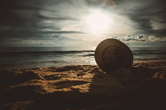 Stylish straw hat on the sand against the backdrop of the sea and sunset sky