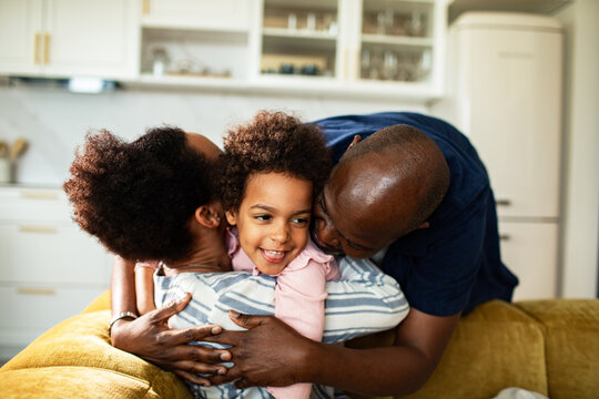 Parents hugging child on sofa in bright home kitchen