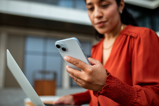Businesswoman using smartphone and laptop outdoors at office