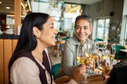 Smiling women friends toasting white wine at a restaurant