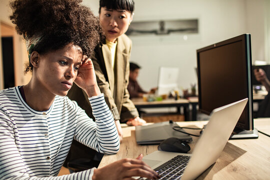 Two coworkers troubleshooting a laptop issue in a modern office