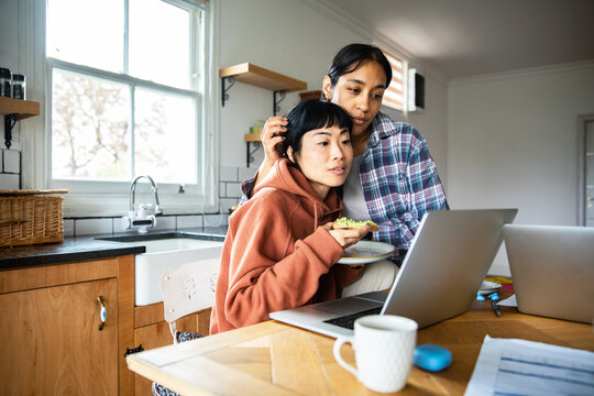 Couple using laptops while eating breakfast in home kitchen