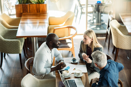 Diverse coworkers reviewing reports in modern cafe