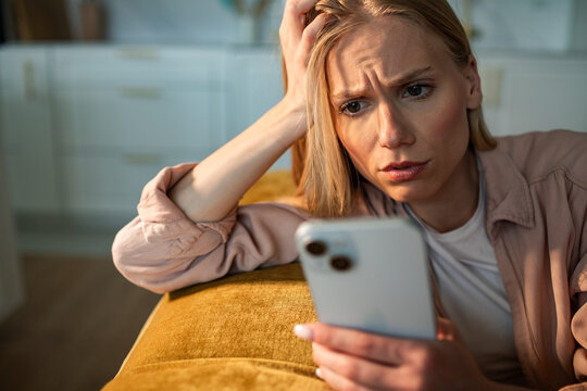 Concerned young woman reading smartphone at home