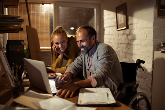Couple with wheelchair user working on laptop in home office at night