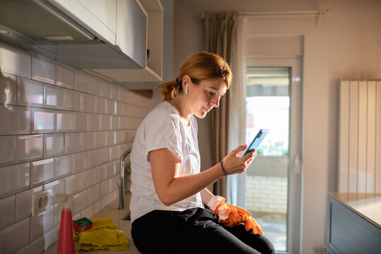 Young woman checking smartphone during cleaning break in modern kitchen