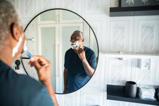 Senior man shaving with razor at bathroom mirror