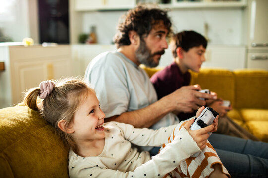 Father and children playing video games on living room sofa