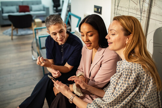 Three businesswomen collaborating on smartphone in modern office