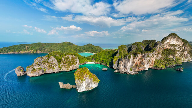 Tropical limestone islands surrounded by deep blue sea water with lush green forests and a hidden white sandy beach in Thailand during a bright summer day