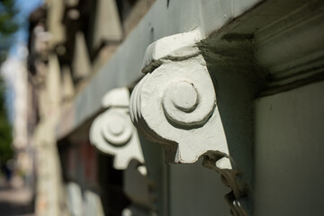 Carved white console brackets repeat along the cornice of an old wooden building, hand-shaped ornament from a period when labour cost less than material. © K