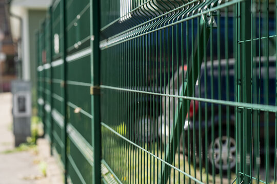 A dark green welded mesh fence runs sharply away from the camera with a parked car softened behind the wire, the cheapest way to define a suburban plot.