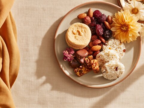Overhead flat lay of traditional Chuseok harvest foods including rice cakes, nuts, dried fruits, and a decorative flower on a beige fabric background