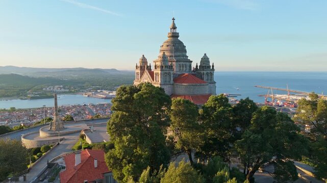 Beautiful aerial reveal of Santa Luzia Sanctuary from behind green trees in Viana do Castelo, Portugal at dawn. Reveal orbit shot.
