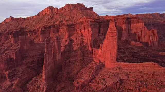 Sweeping sunset flight reveals towering Cutler sandstone Fisher Towers spires and rugged desert canyons bathed in warm evening light near Moab Utah