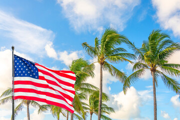 Obraz premium American flag waving against palm trees on blue sky background