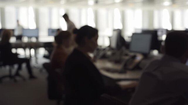 Intentionally blurred professionals work at computer stations in a bright open-plan office. Business presentations, corporate communications, and recruitment campaigns.