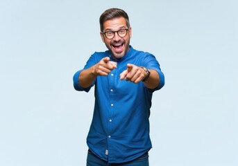 Fototapeta premium Excited middleaged man with glasses wearing a blue shirt pointing directly at the camera with both hands, expressing joy and enthusiasm against a light background