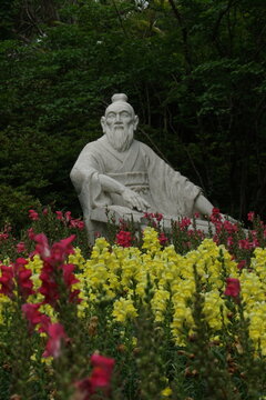 Traditional Chinese philosopher stone sculpture playing guqin surrounded by colorful flowers in a forest garden at Erling Park, China