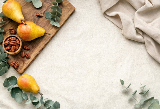 Fresh pears and pecans on a wooden board with eucalyptus leaves on a linen background