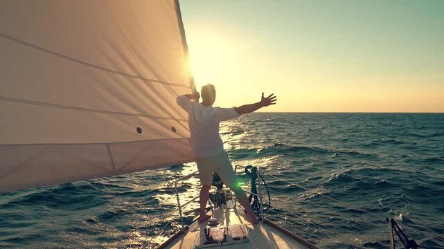 Ships captain sailing across ocean, raising hands. Yacht with sail gliding sea, man on deck gazing sun. Sail towards your dream, adventure. Man sailing on yacht under white sail. Sea voyage free wind