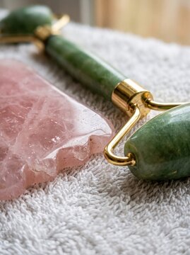 Macro of pink quartz gua sha scraper and green jade facial roller on soft white towel, natural skincare, spa beauty routine.