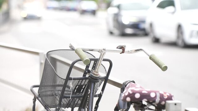 A parked city bicycle rests against a street railing while traffic passes behind it, the everyday overlap of cycling and driving on one shared street.