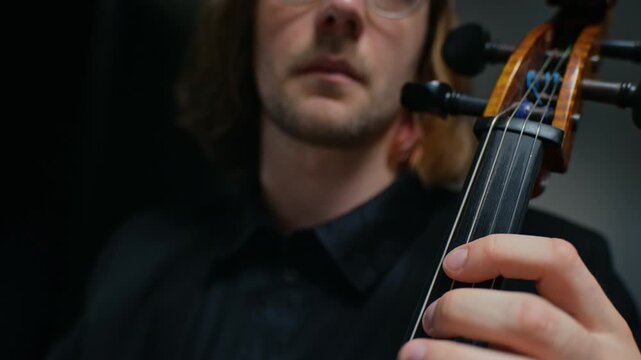 Caucasian young adult man playing cello, camera tilting up from close up of hand on fingerboard to face. Footage ideal for classical music school promos or concert advertisements