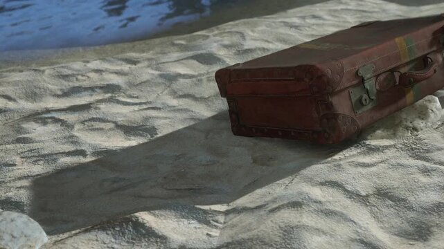 A suitcase lies on the sand close to the water. It appears weathered and abandoned. The beach scene features light waves and a clear sky. The area is quiet with soft textures.