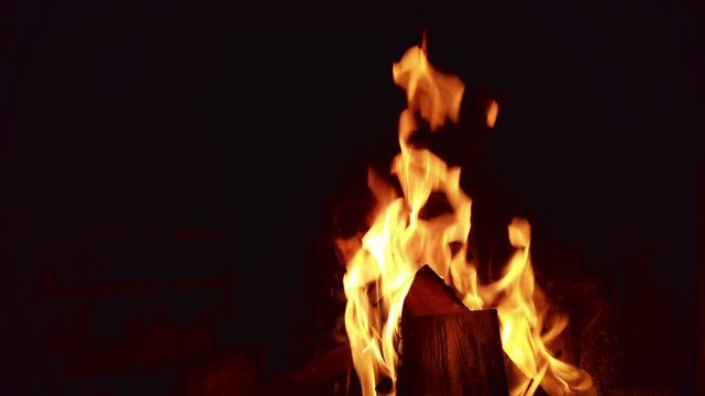 Fire burns wood in dark space for several moments showcasing bright flames and smoke rising above as the wood starts to break down and turn to ash